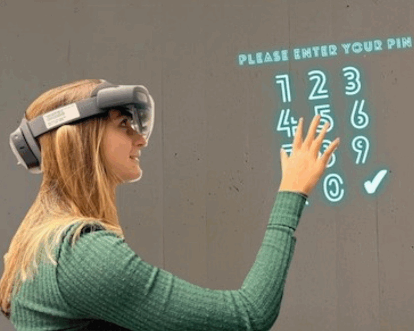 Eine junge Frau trägt eine HoloLens-Brille und tippt auf einem projizierten Zahlenfeld eine PIN ein.